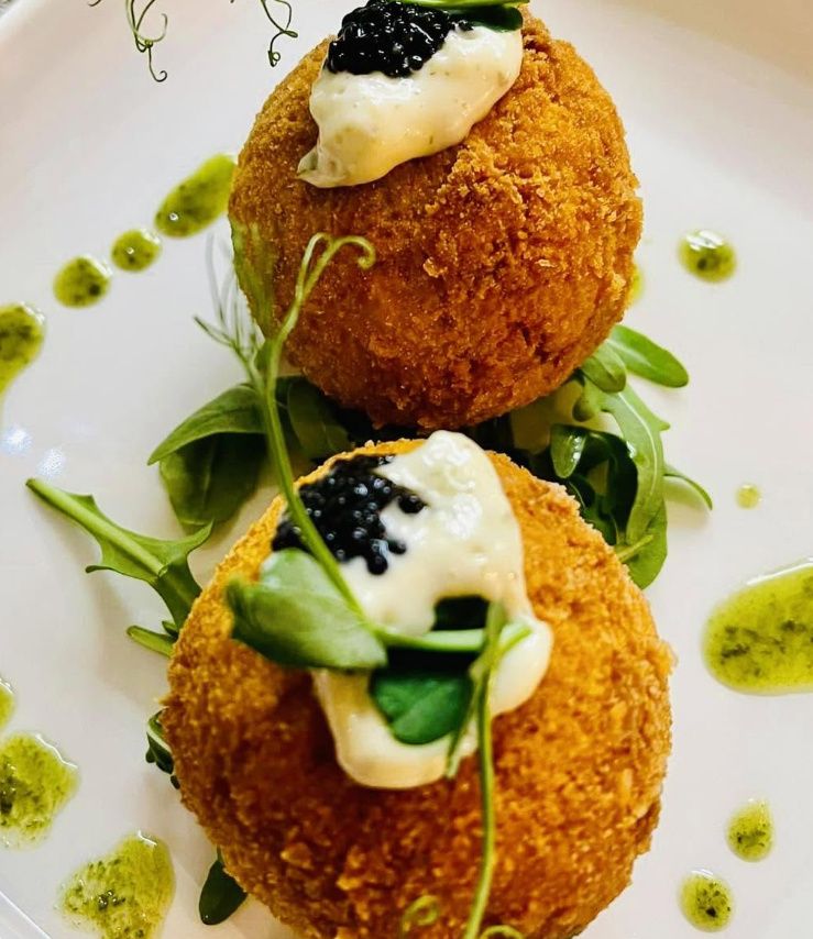 Two golden breaded croquettes topped with aioli and black caviar, on rocket with drops of herb oil
