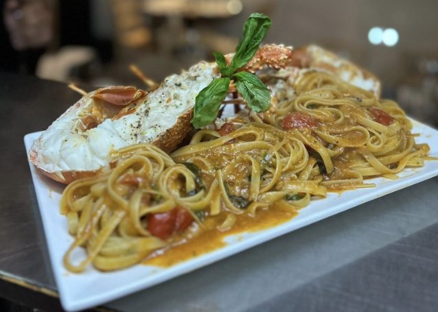 Linguine in a lobster and cherry tomato sauce served with a halved lobster and fresh basil on a white platter