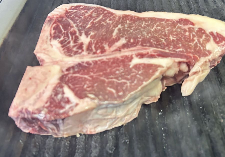 A thick raw marbled T-bone steak resting on a grill plate before cooking