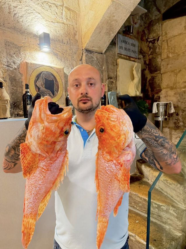 A staff member presenting a fresh whole red fish to the table