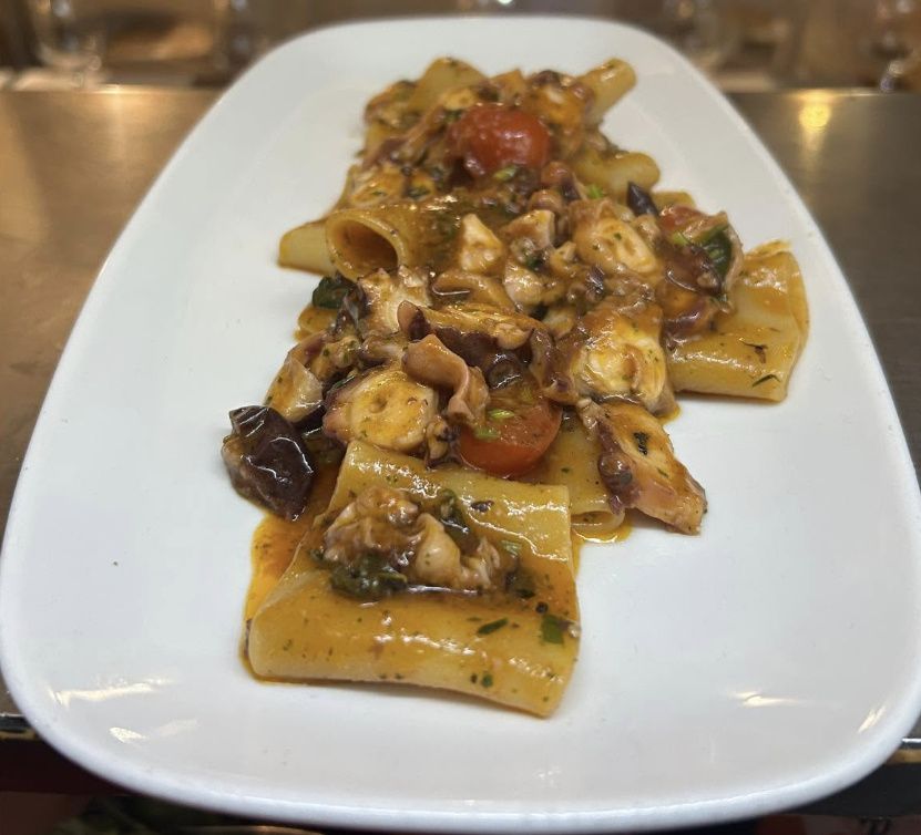 Paccheri pasta with octopus, cherry tomatoes and black olives in a light tomato sauce on an oval white plate